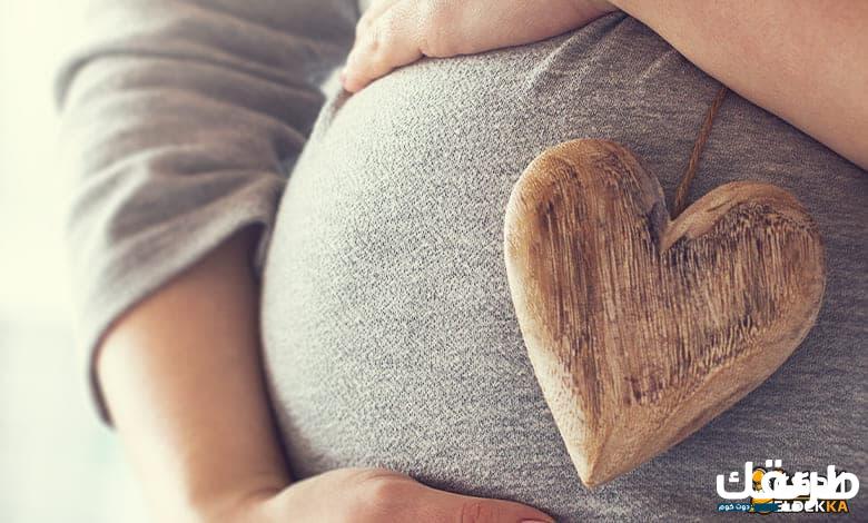 pregnant woman holding heart while touching her belly 1